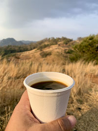 Cropped hand holding coffee on field