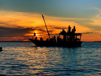 Silhouette people in sea against sky during sunset