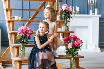 Siblings sitting amidst flowers in vase on wooden steps at home