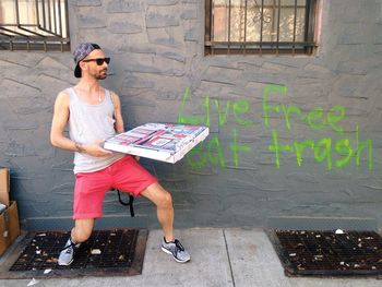 Full length of man with box standing against text on wall