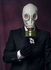Portrait of man wearing gas mask while holding flower against black background
