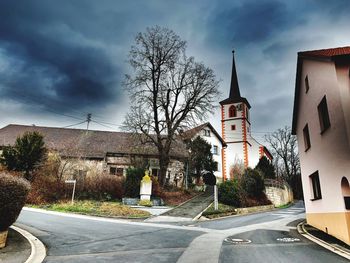 Road by buildings against sky