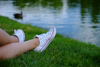 Low section of person legs on field by lake