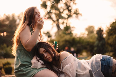 Young woman blowing bubbles while her girlfriend lying on her leg