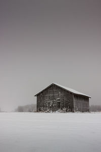Snow covered barn by field against clear sky