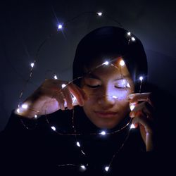 Close-up of young woman wearing hijab holding illuminated string light in darkroom