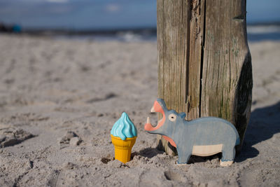 Close-up of toys by wooden post on sand at beach