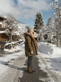 Side view of young woman wearing warm clothing standing on road during winter