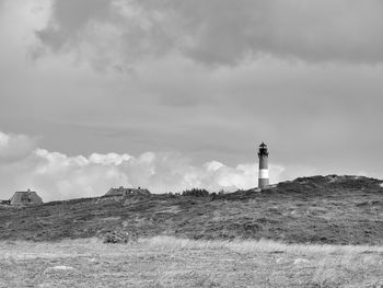 Lighthouse on field by building against sky