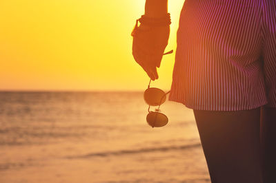 Rear view of woman with arms raised against sea during sunset