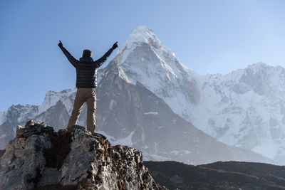 Man standing on rock by snowcapped mountain against sky