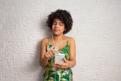 Young woman using phone while standing against wall