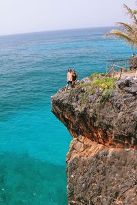 Men standing on rock formation over sea against sky