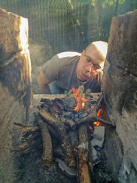 Low angle view of man relaxing on wooden log, preparing bbq 