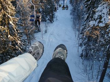 Legs against overhead cable cars at snowed landscape