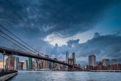 Low angle view of brooklyn bridge over river against cloudy sky in city