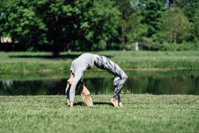 Full length of young woman exercising by pond on field