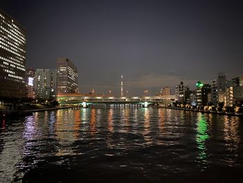Illuminated buildings by river against sky at night