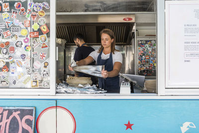 Confident young female owner holding foil against colleague working in food truck