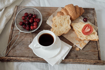 Tasty breakfast with fresh croissant, coffee, cherries on a wooden tray. hearty croissant 