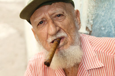 Close-up portrait of senior man wearing cap smoking cigar