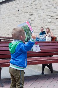 Side view of boy reading newspaper while standing on bench