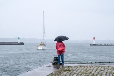 Woman with umbrella standing at beach against sky