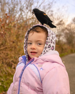 Portrait of cute girl with bird perching on head against plants