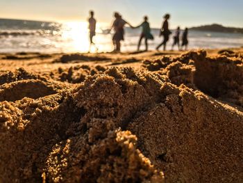 People standing on beach against sky during sunset