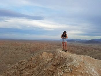 Front view of young woman standing on desert landscape against sky