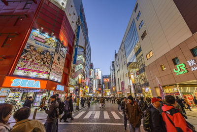 People walking on illuminated street lights in city against sky