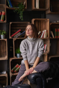 Thoughtful woman sitting against shelf