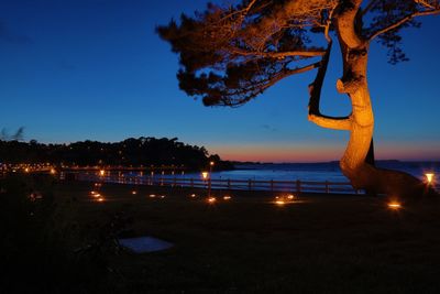 Illuminated lights at promenade by sea against blue sky during sunset