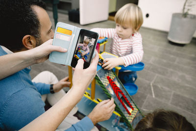 Cropped hands of mother photographing daughter playing with toy cars on porch