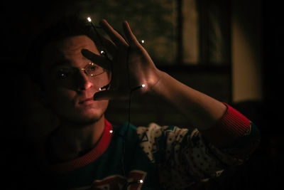 Close-up of young man holding illuminated lights in darkroom