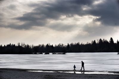 Silhouette people walking on frozen field during winter