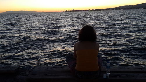 Rear view of silhouette woman standing at beach during sunset