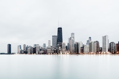 Sea by modern buildings against sky in city