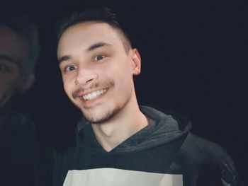 Portrait of smiling young man against black background