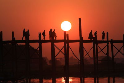 Silhouette people on u bein bridge over river during sunset