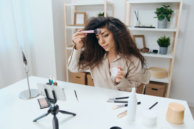 Woman filming make-up tutorial through smart phone on tripod at home