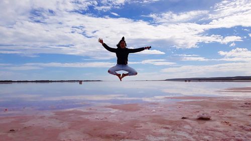 Woman jumping at beach against sky