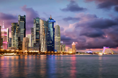 Illuminated city by sea against sky