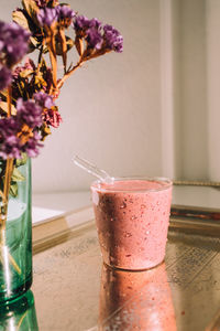 Pink mixed berry smoothie with glass straw on silver tray with dried flowers