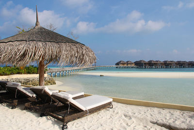 Lounge chairs by swimming pool at beach against sky