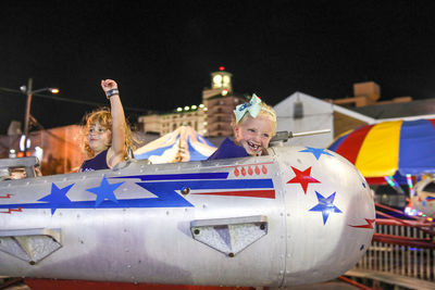 Two girls on carnival ride at night in summer hand in the air laughing