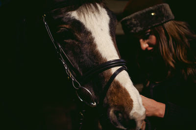 Woman adjusting horse bridle while standing outdoors at night