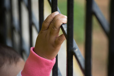 Cropped image of child hand holding metal grate