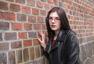 Young beautiful girl in black jacket and jeans stands near the old fortress wall on sunny day