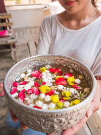 Midsection of woman holding bowl with water and petals